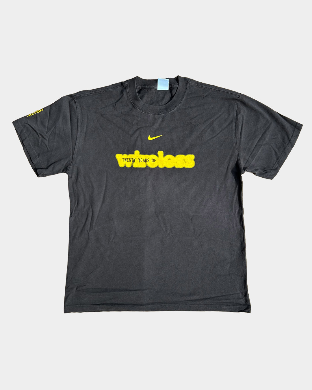 The Wireless Festival 20th Anniversary Nocta x Drake x Wireless T-Shirt is black, with yellow TWENTY YEARS OF text and a blurred word below, a small yellow Nike logo above, and yellow writing on the left sleeve.